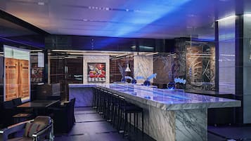 Un espace bar moderne doté d’un comptoir en marbre, de tabourets de bar et d’un élément décoratif central.