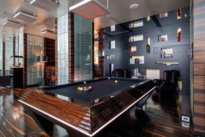 A modern pool table with a sleek design, surrounded by bookshelves and seating areas.