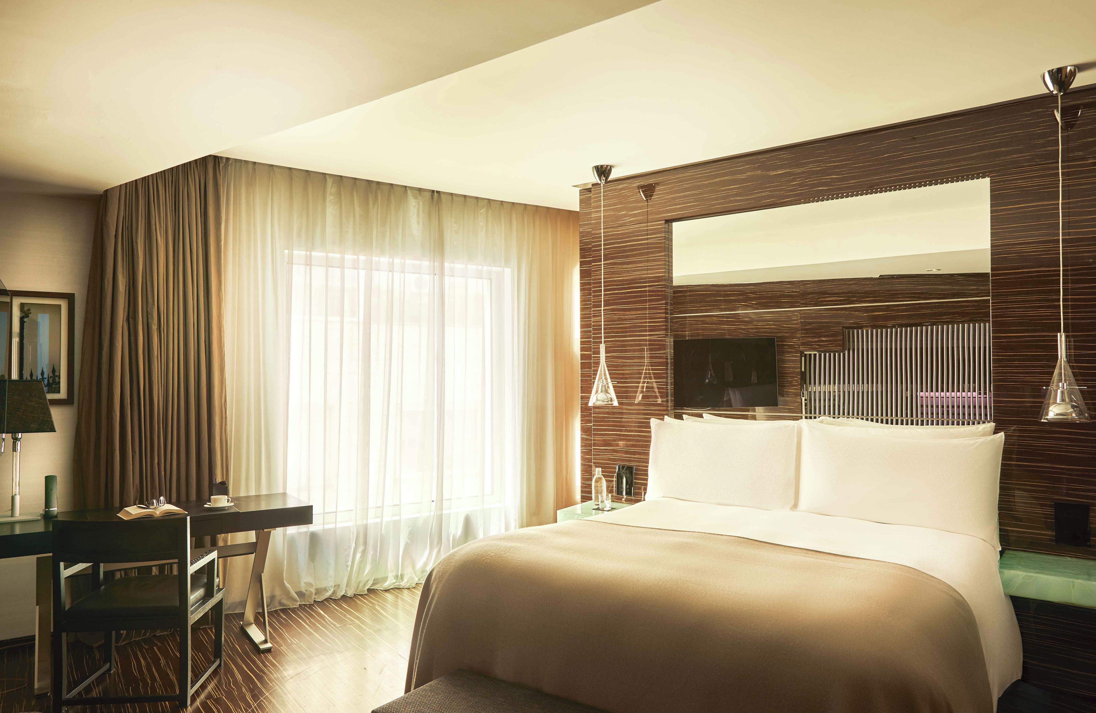 Una habitación de hotel con una cama grande, un escritorio, una silla, un televisor y un ventanal con cortinas.
