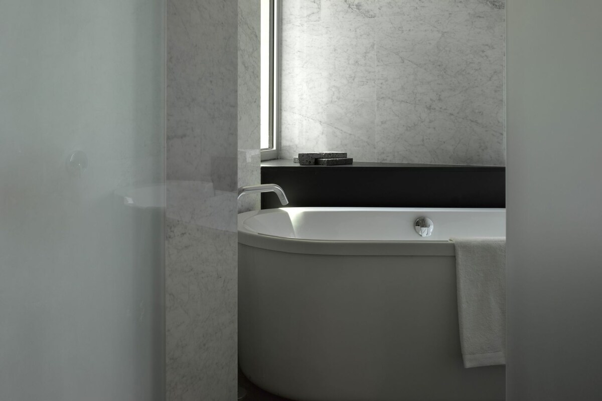 Un baño moderno con una bañera independiente, una ventana y una encimera oscura.