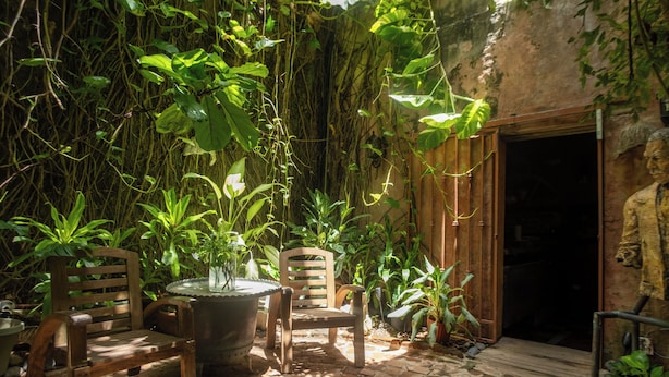 An outdoor patio with wooden chairs and a table, surrounded by lush greenery and a rustic stone floor. - The Gallery Inn (San Juan)
