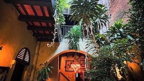 An indoor courtyard with a staircase leading to an upper level, surrounded by potted plants and a chandelier. - The Gallery Inn (San Juan)