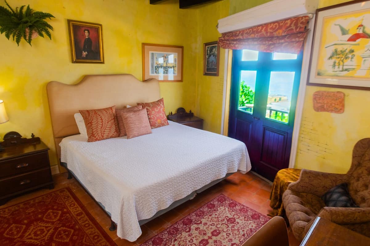 A bedroom with a bed, a nightstand, a chair, a window with a view, and a door.