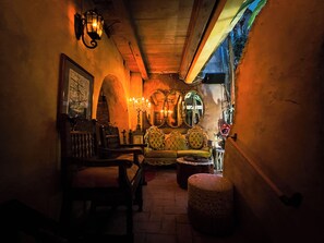 A dimly lit room with a vintage sofa, a wooden chair, and a patterned ottoman.