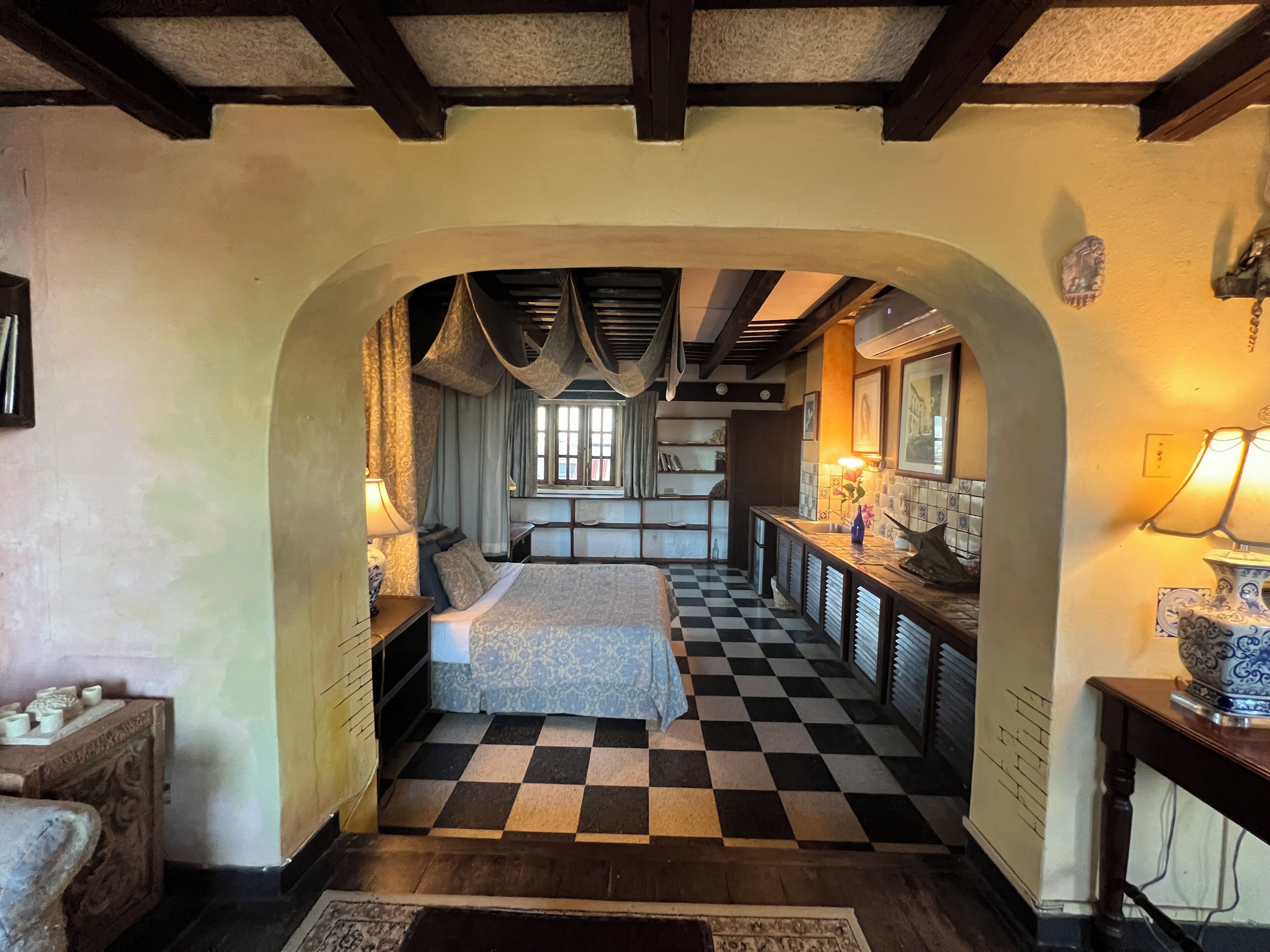 A bedroom with a checkered floor, a bed, and a window with curtains.
