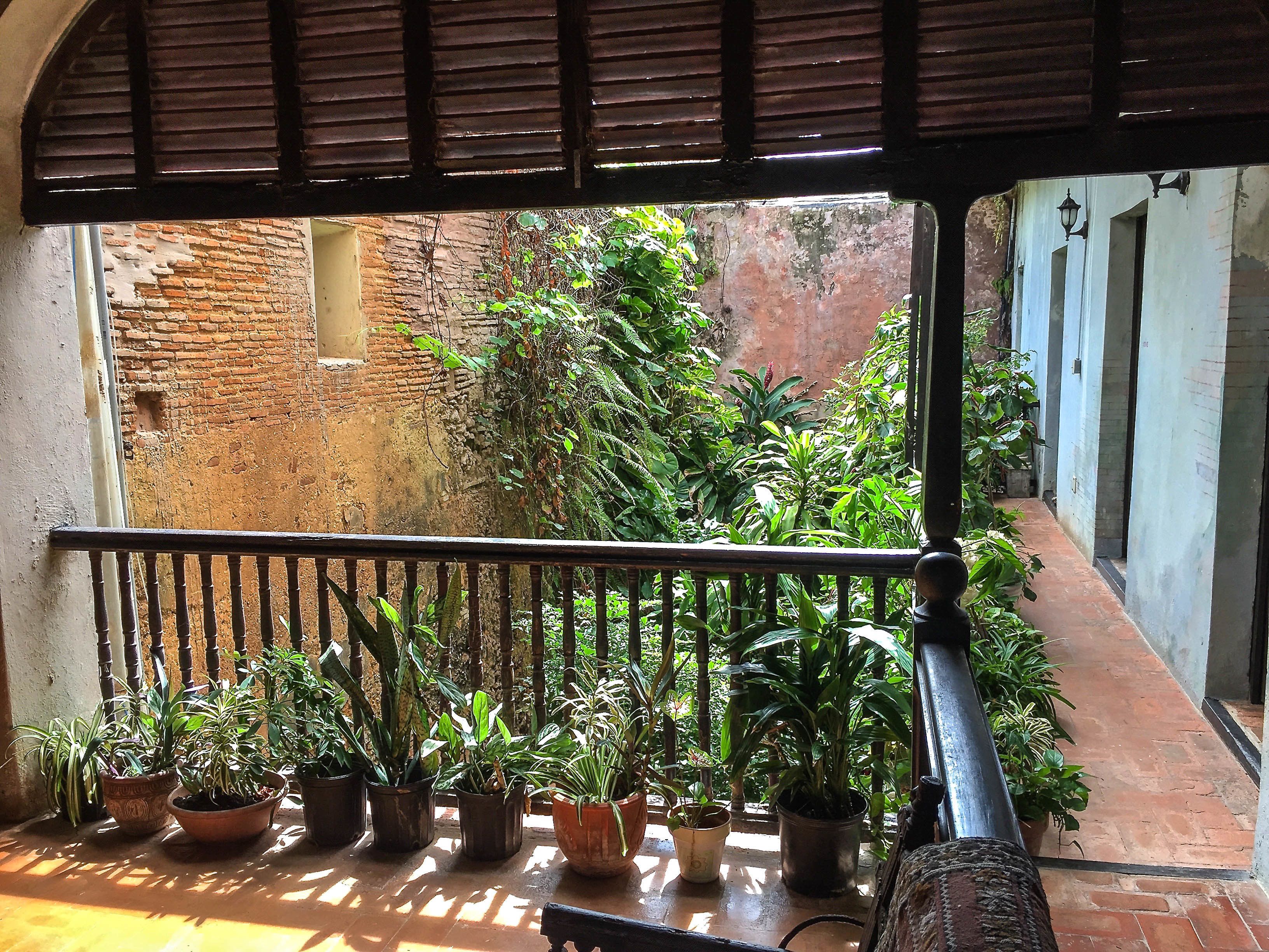 A balcony with a view of a brick wall and lush greenery.