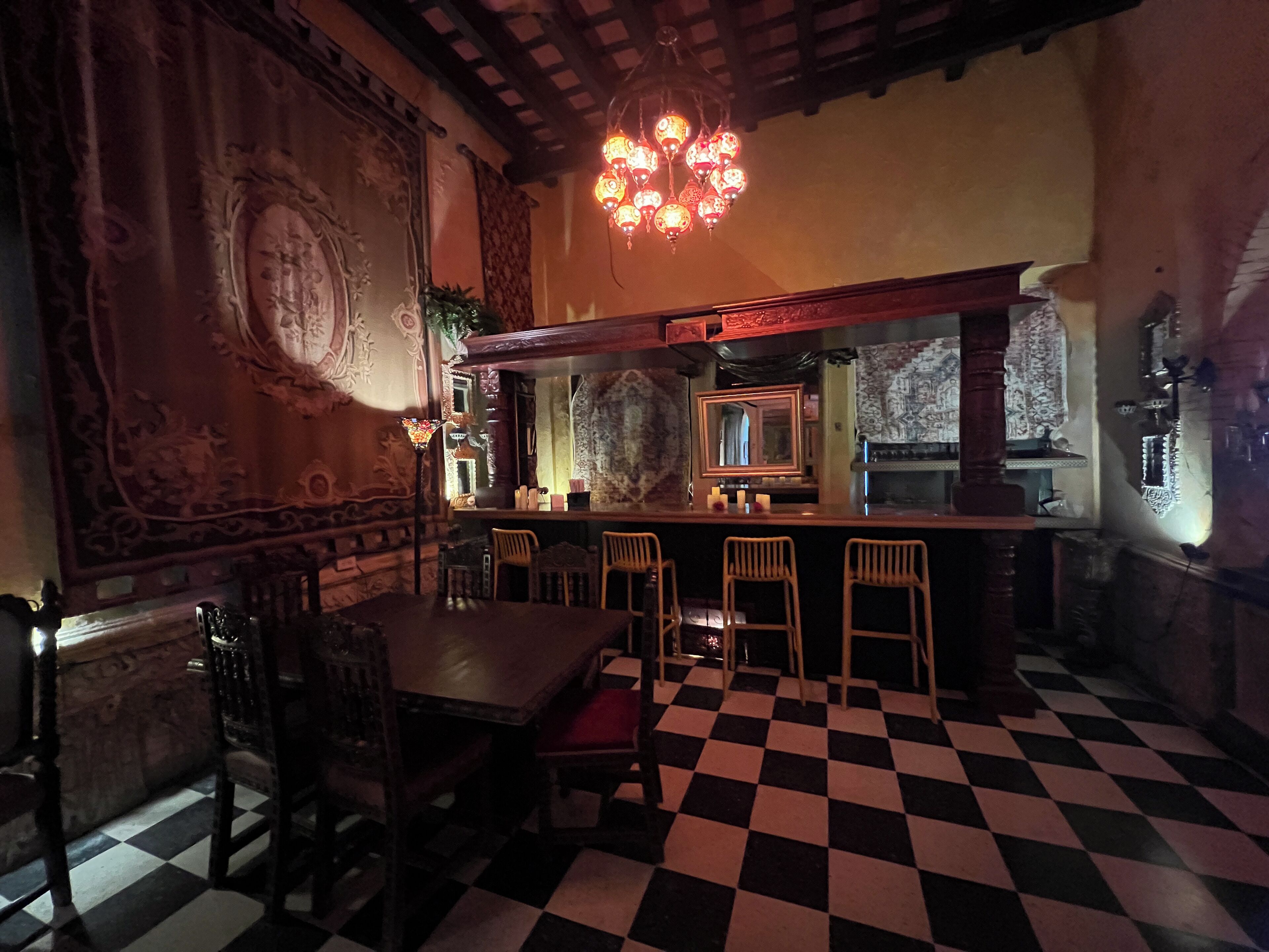 A bar area with a checkered floor, bar stools, and a large mirror above the bar.