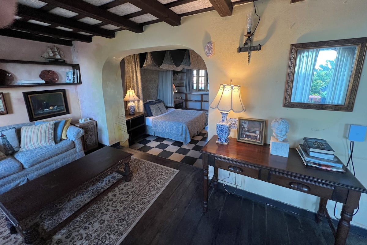 A cozy room with a checkered floor, a sofa, a wooden table, and a bed with a canopy.