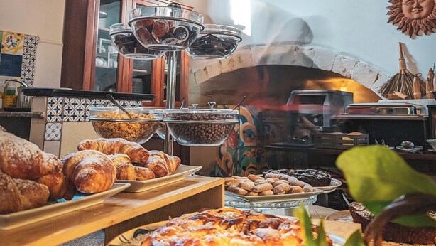 A buffet with various baked goods and a pizza on a wooden table. - La Corte Del Sole (Noto)