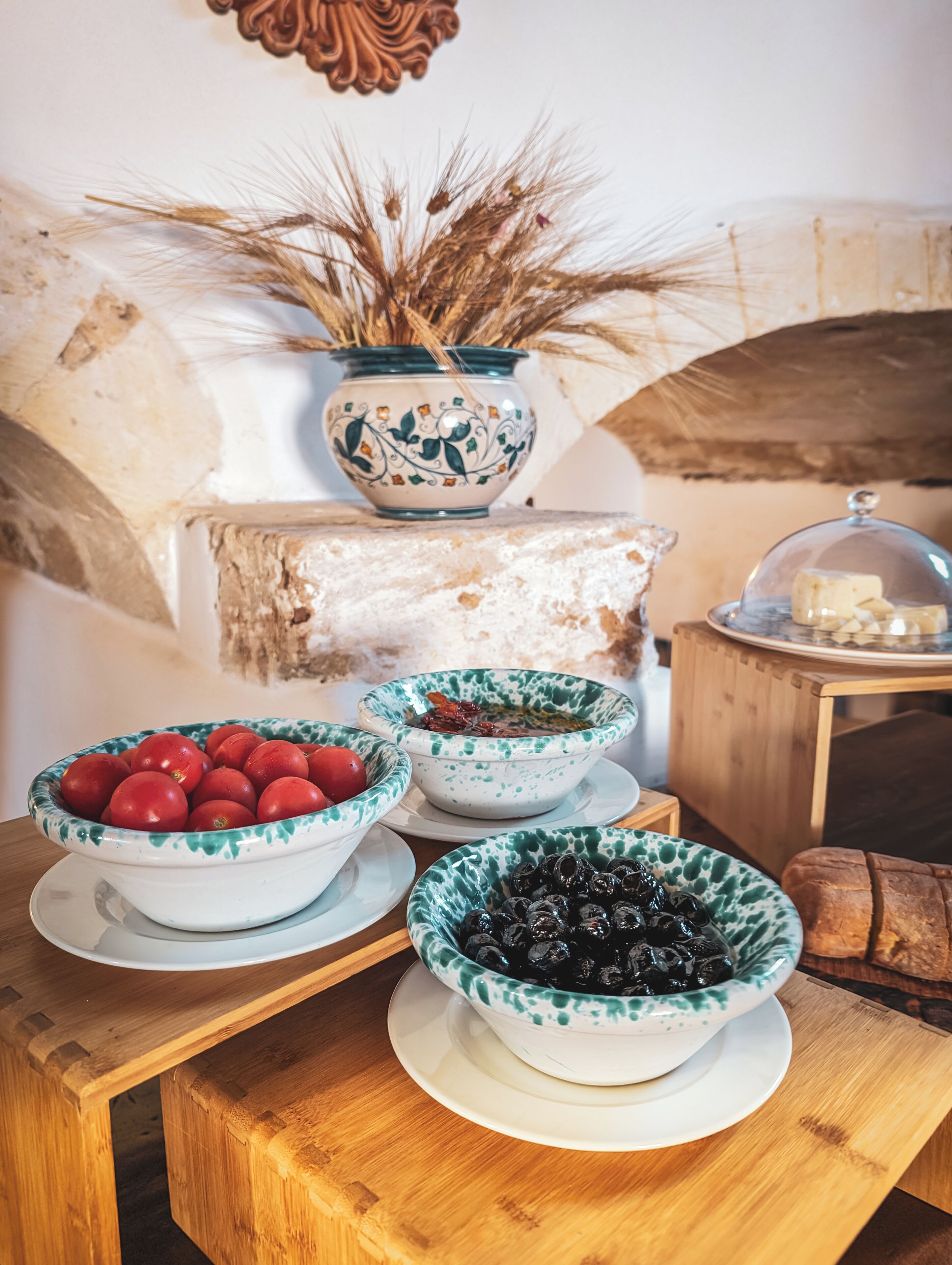 A wooden table with three bowls of food, a decorative vase, and a cheese display.