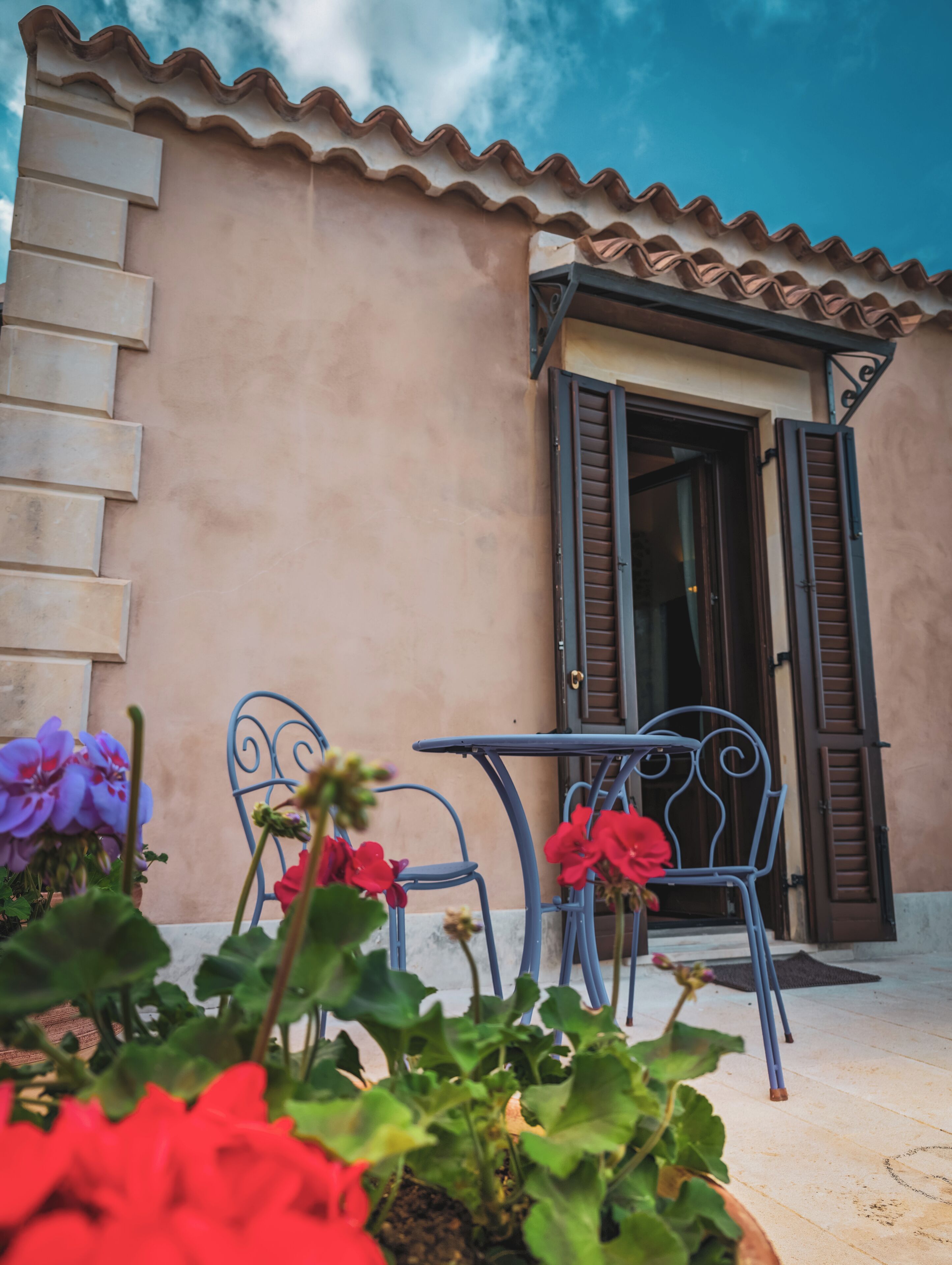 A building with a tiled roof, a door with shutters, and a table with chairs outside.