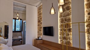 A modern bedroom with a bed, bedside table, and a TV mounted on a stone wall. - La Corte Del Sole (Noto)
