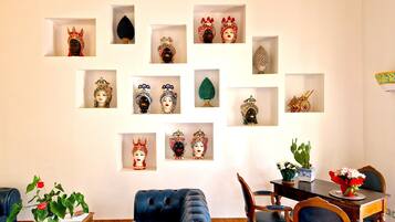 A living room with a blue sofa, a dining table with chairs, and a wall decorated with various cultural artifacts in display cases.