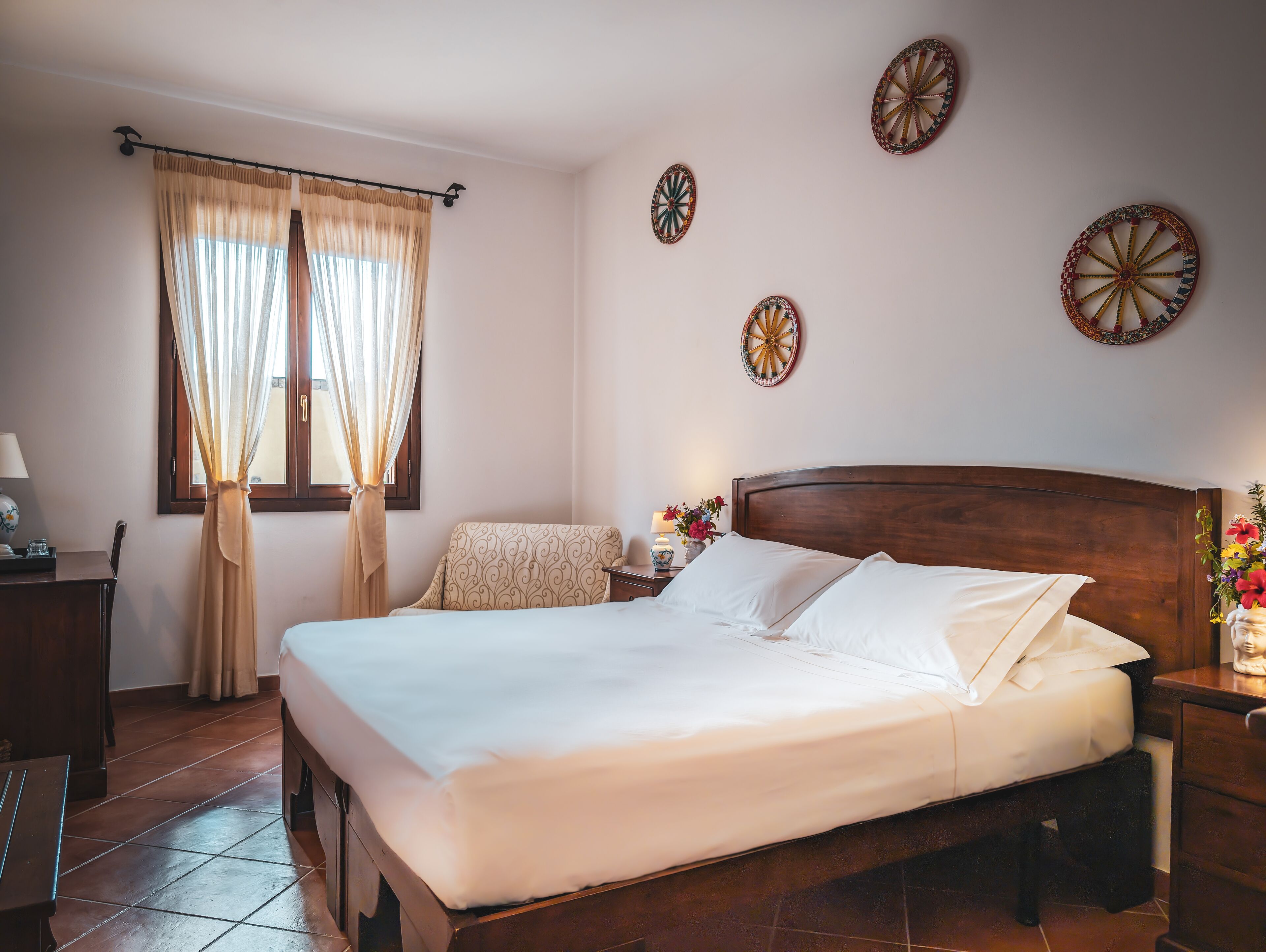 A neatly made bed with white linens, a wooden headboard, and a bedside table with a lamp and flowers.