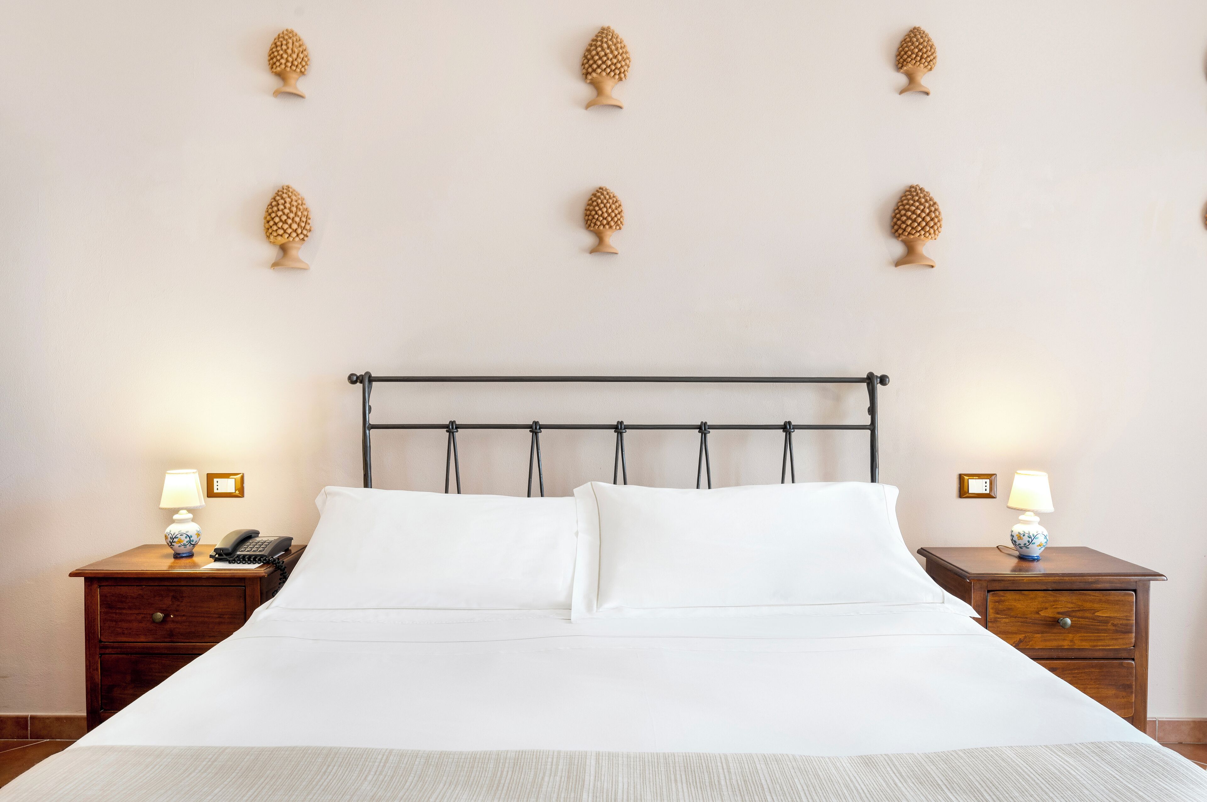 A neatly made bed with white linens, a wooden headboard, and two bedside tables with lamps and a phone.