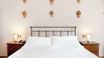 Een net opgemaakt bed met witte lakens, een houten hoofdbord en twee nachtkastjes met lampen en een telefoon.