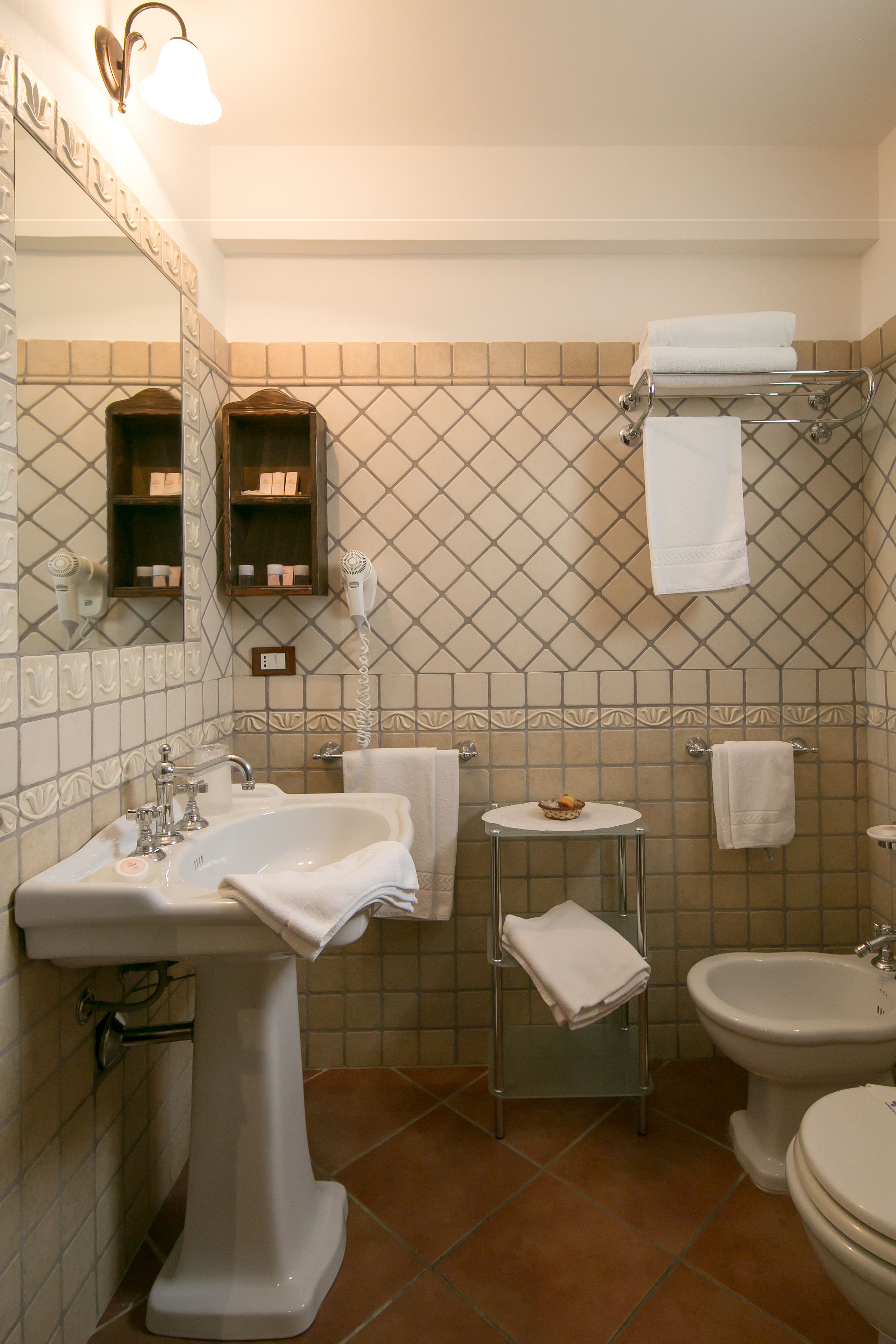 Casa de banho com lavatório suspenso, bidé, sanita e uma pequena mesa com uma toalha, e um porta-toalhas.