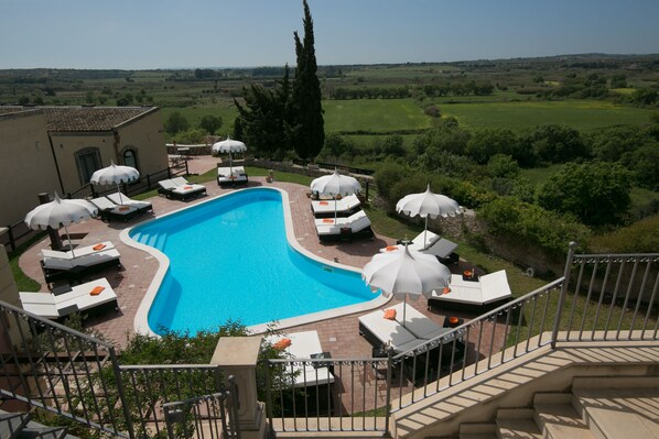 A pool area with lounge chairs and umbrellas, surrounded by a scenic landscape.