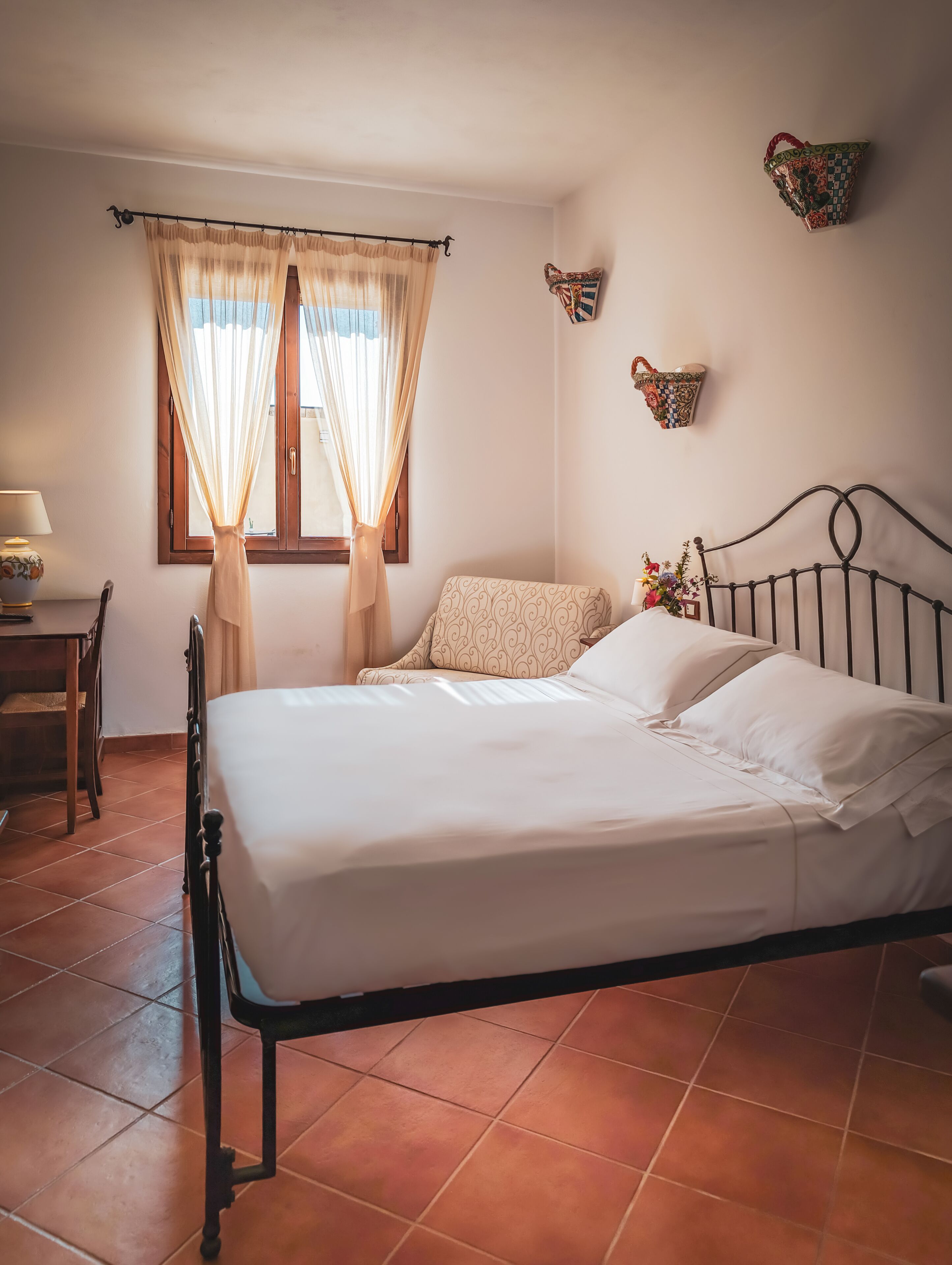 Una cama bien tendida con sábanas blancas, cabecera de madera y ventana con cortinas de gasa.