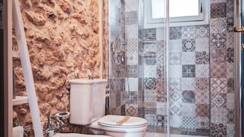 Une salle de bain avec un mur en pierre, deux toilettes, une douche avec une porte en verre et un sol carrelé.