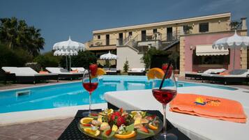 A poolside setting with lounge chairs, a fruit platter, and two glasses of red wine.
