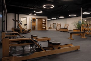 Academia com equipamento de exercícios, mobiliário de madeira e um espelho grande.