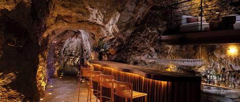 Una zona de bar con mostrador de madera, taburetes y suelo de piedra.