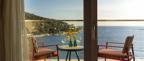 A balcony with two chairs and a table, overlooking a coastal landscape with buildings and the sea.