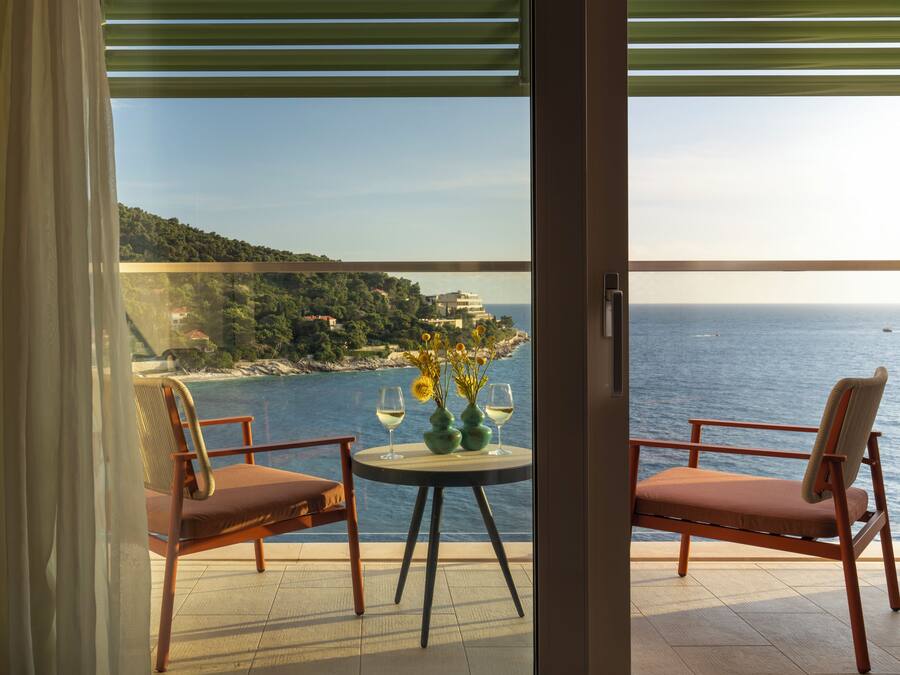 Un balcón con dos sillas y una mesa, con vistas a un paisaje costero con edificios y el mar.