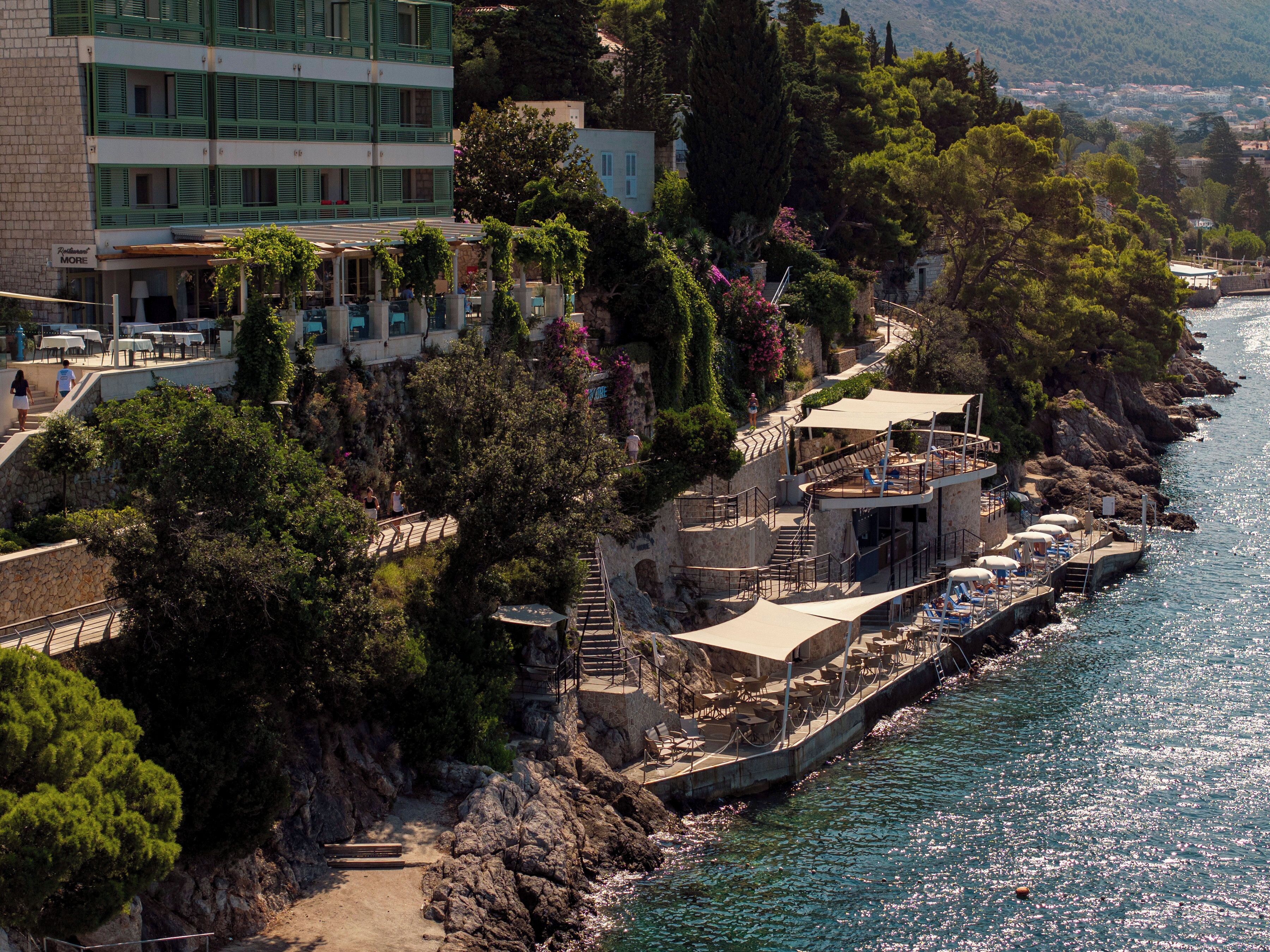 Un hotel frente al mar con terraza exterior, una escalera que conduce a los pisos superiores y vistas del paisaje circundante.
