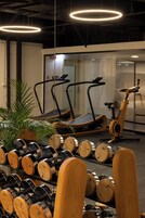 Uma academia com equipamentos de exercício, incluindo esteiras e um elíptico, e um suporte com halteres.