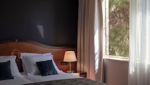 A hotel room with a bed, pillows, a nightstand with a lamp, and a window with curtains.