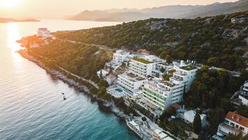 A coastal hotel with multiple buildings, a swimming pool, and a pier.