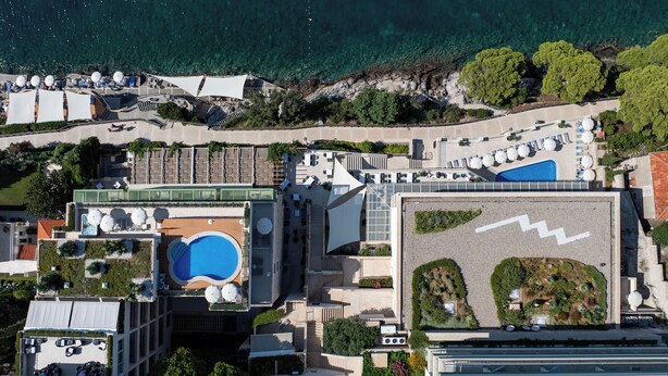 An aerial view of a hotel with a rooftop pool, outdoor seating, and a landscaped garden.