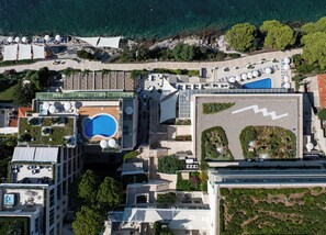 Vista aérea de um hotel com piscina no terraço, área de estar externa e um jardim paisagístico.