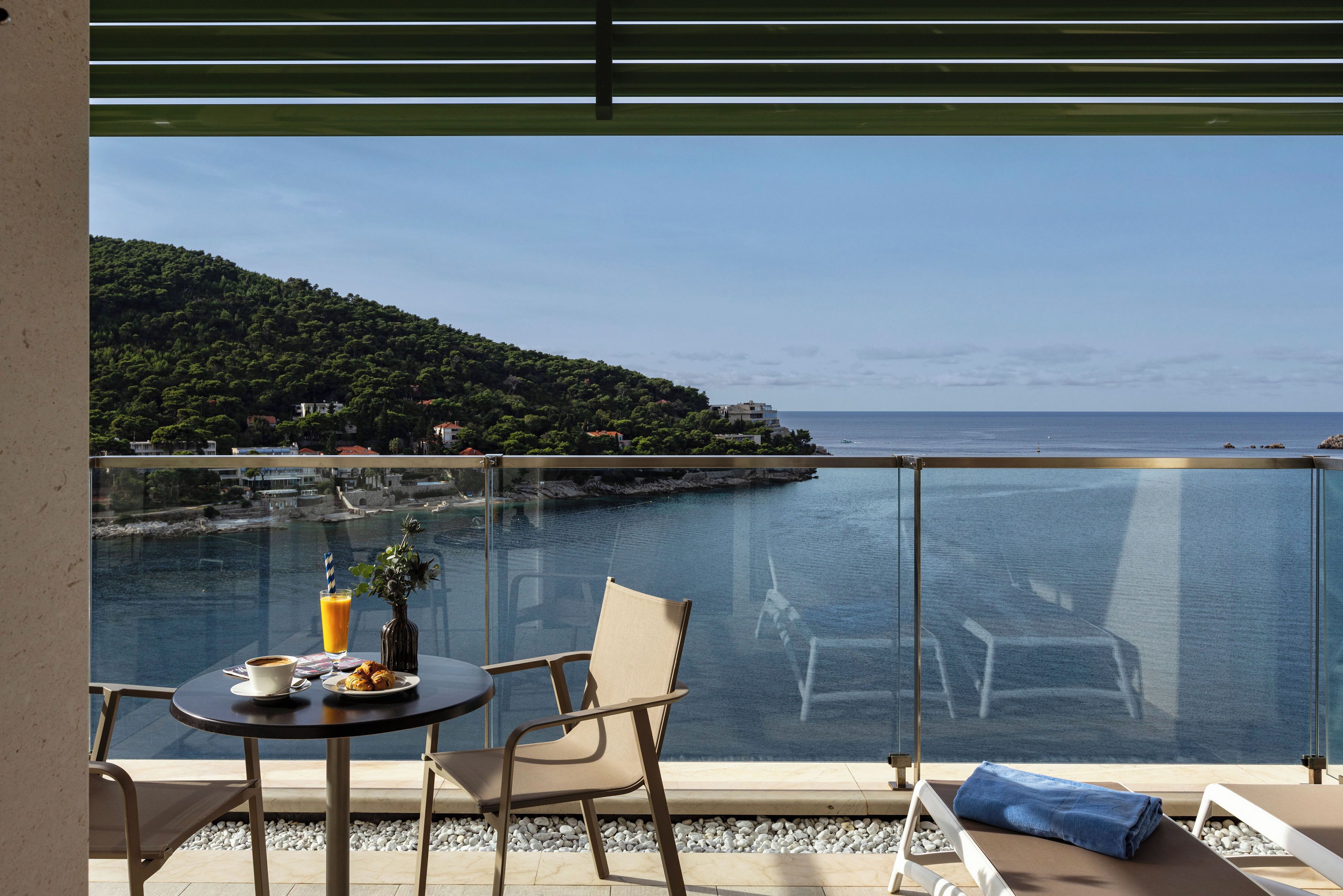 Un balcón con mesa, sillas y vista al mar y a una colina.