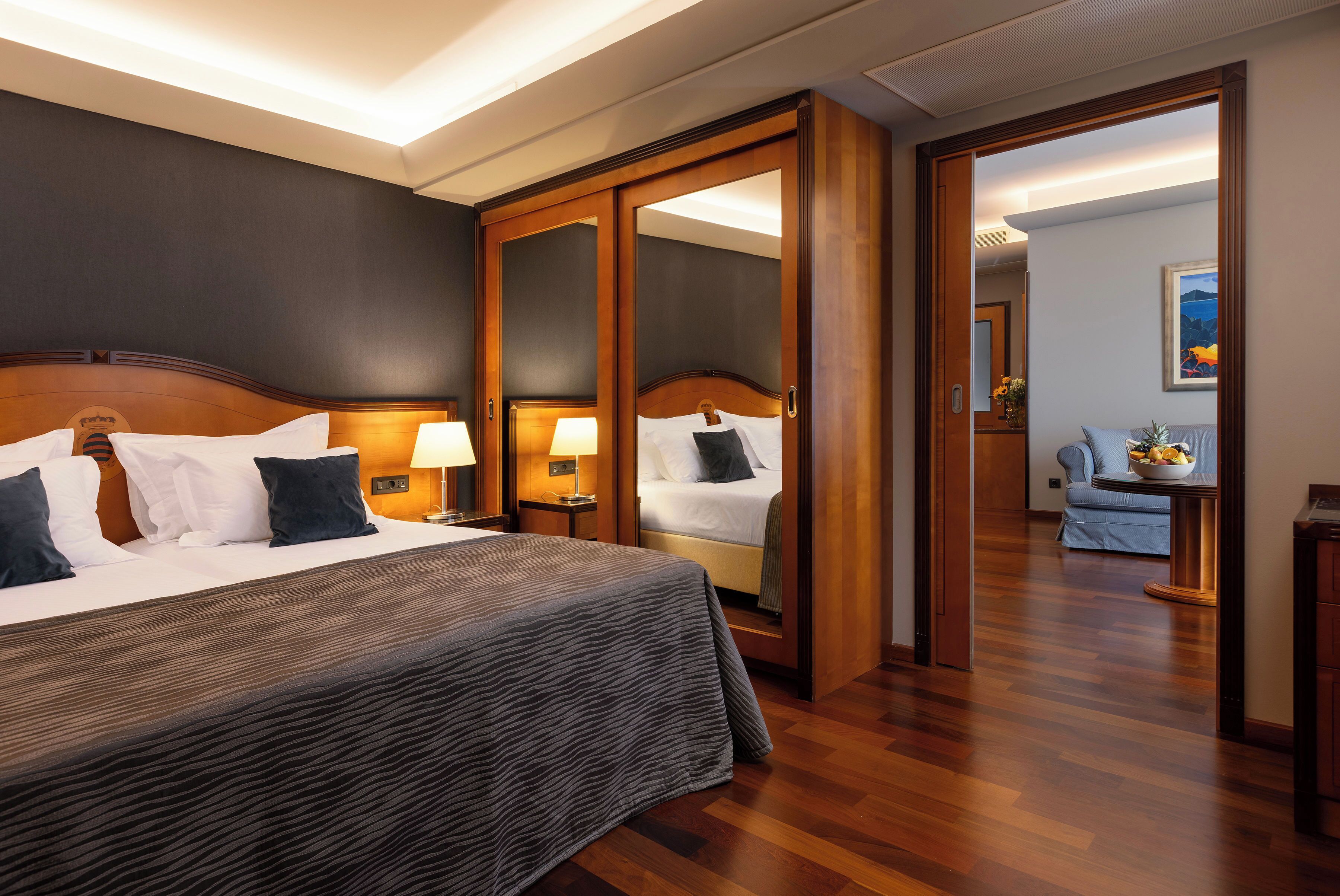 Quarto de hotel com uma cama grande, um guarda-roupa, uma escrivaninha com luminária e um quadro na parede.