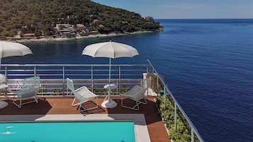 Terraço com piscina, espreguiçadeiras e guarda-sóis com vista para a costa.