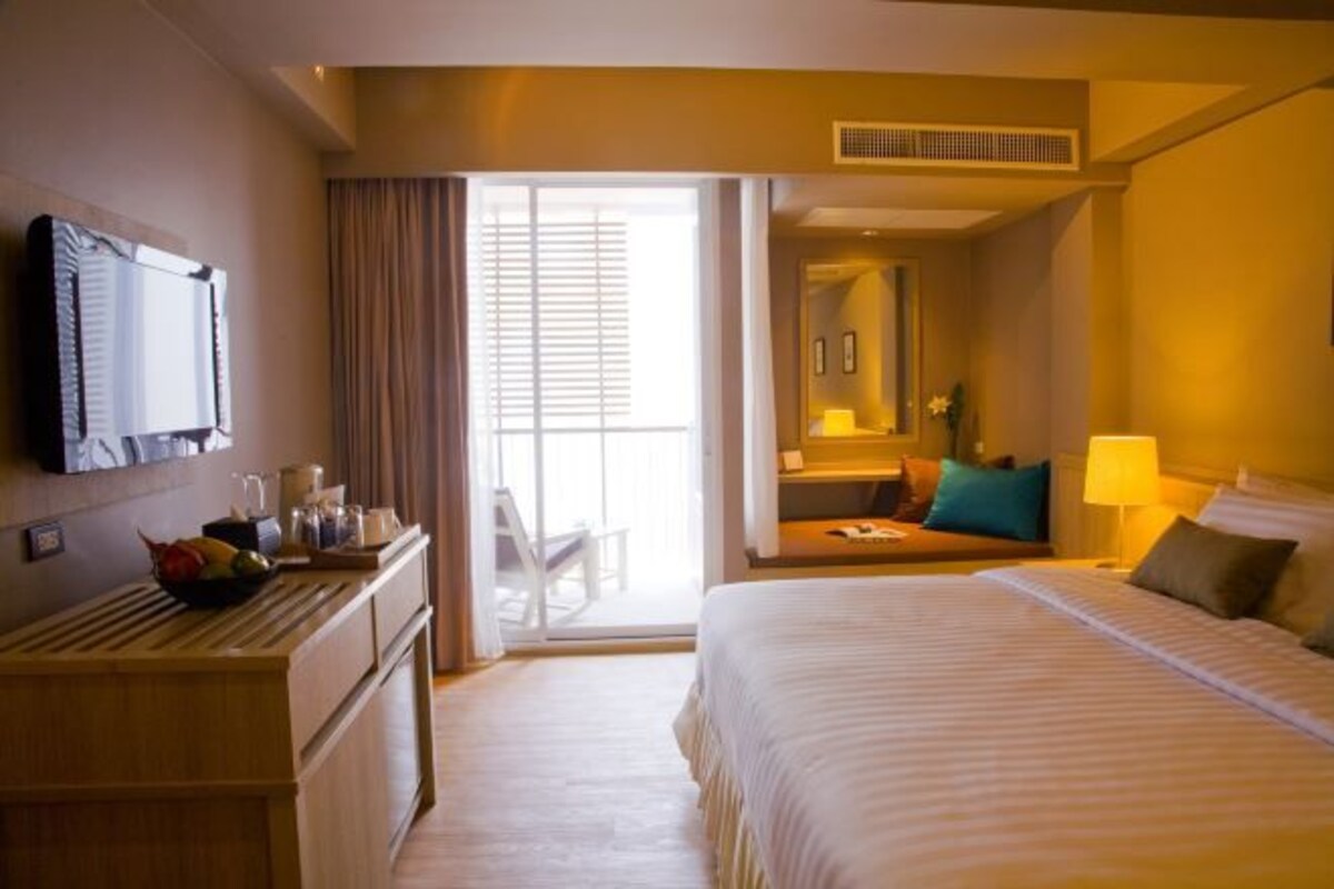 Habitación de hotel con cama, escritorio con computadora, silla, mesita de noche con lámpara y ventana con cortinas.