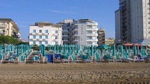 A beach with rows of sun loungers and umbrellas, a building labeled "HERON," and other residential buildings in the background.