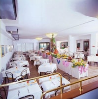 A spacious dining area with multiple tables and chairs, air conditioning units on the ceiling, and a staircase leading to an upper level.