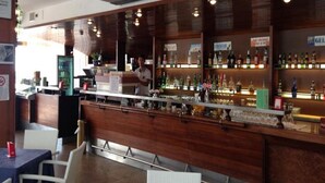 A bar area with a wooden counter, shelves of bottles, and a person standing behind the bar.