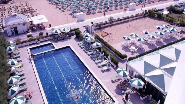 A resort with a swimming pool, beach umbrellas, and lounge chairs.