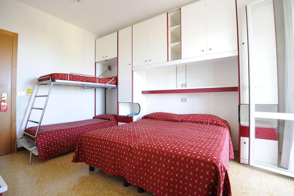 Ein Schlafsaalzimmer mit zwei Etagenbetten, einer Himmelsleiter, einem Schreibtisch und einem Kleiderschrank.