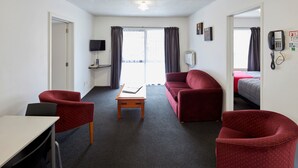 A hotel room with a red sofa, a wooden coffee table, a TV, and a phone on the wall. - Aotea Motel (Christchurch)