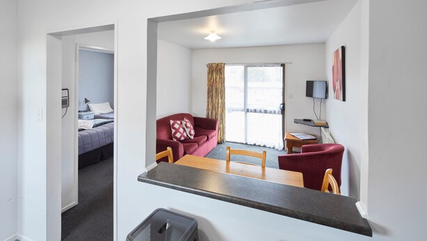 A room with a bed, a red sofa, a wooden dining table, and a TV on the wall. - Aotea Motel (Christchurch)