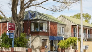 A two-story motel with a red brick facade, a balcony on the second floor, and a blue awning over the entrance. - Aotea Motel (Christchurch)