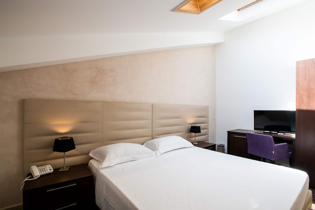 Une chambre d’hôtel moderne dotée d’un grand lit, d’un téléviseur à écran plat, d’un bureau et d’un téléphone sur la table de chevet.