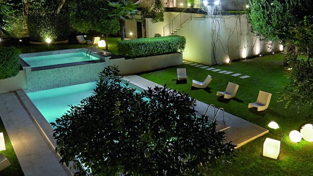 A well-lit outdoor pool area with lounge chairs and a staircase leading to a building.