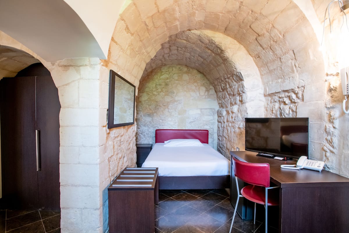 Une chambre avec une arche en pierre, un lit avec une tête de lit rouge, un bureau avec une chaise, une télévision et un téléphone.